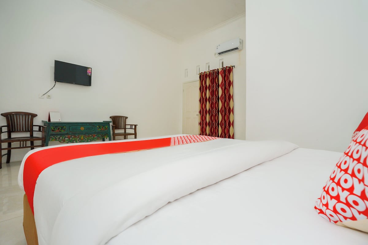 Habitación de hotel con cama, televisor montado en la pared, escritorio con sillas y armario.