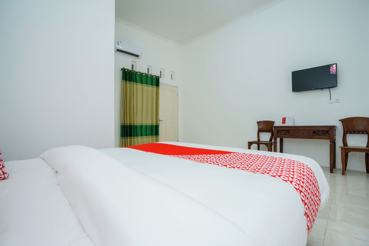 A hotel room with a bed, a desk, a chair, a television, and an air conditioning unit.