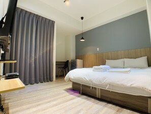 Ein Hotelzimmer mit einem Bett, einem Schreibtisch, einem Stuhl, einem Fernseher und einem Vorhang.