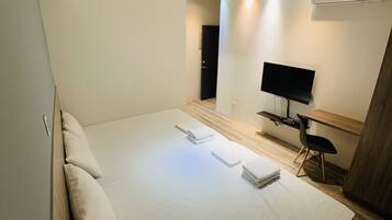 A modern hotel room with a large bed, a desk with a computer, a TV, and a chair.