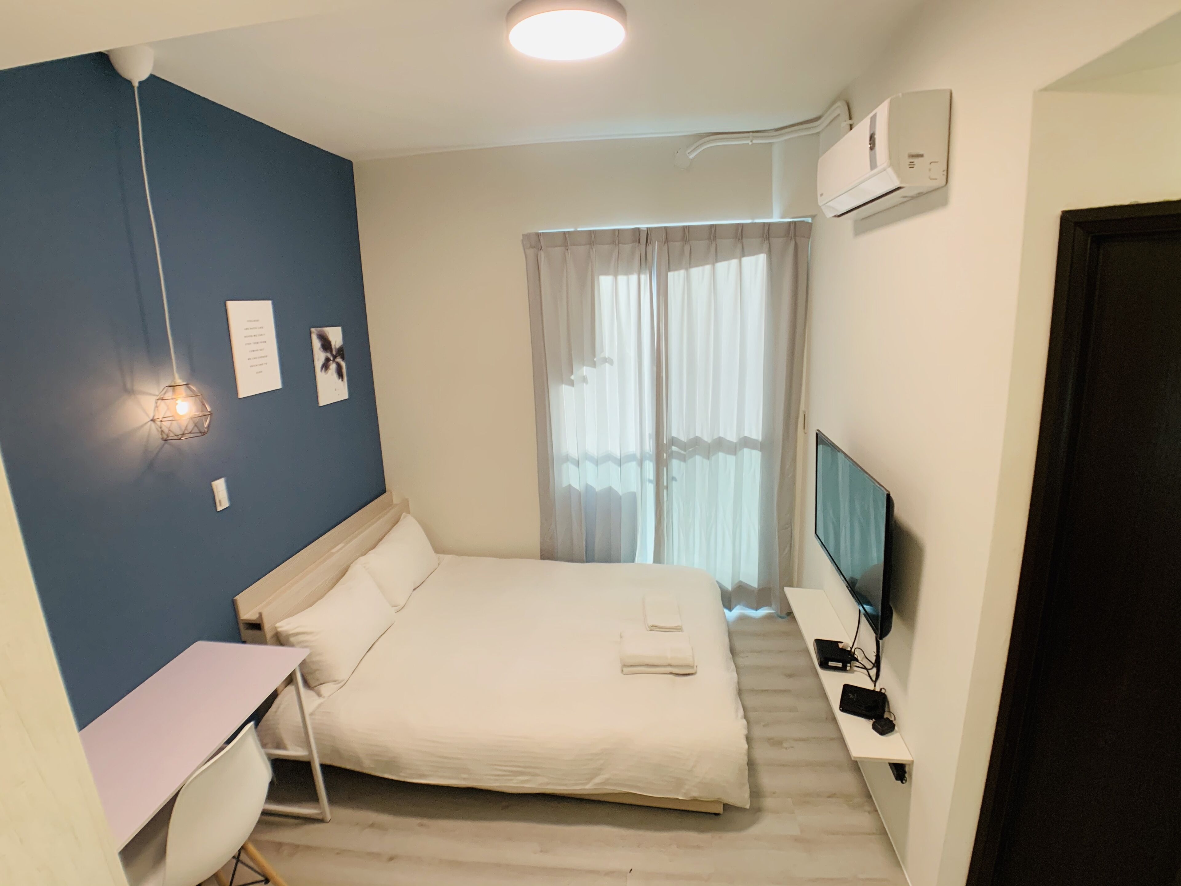 Un dormitorio con cama, escritorio, televisor y ventana con cortinas.
