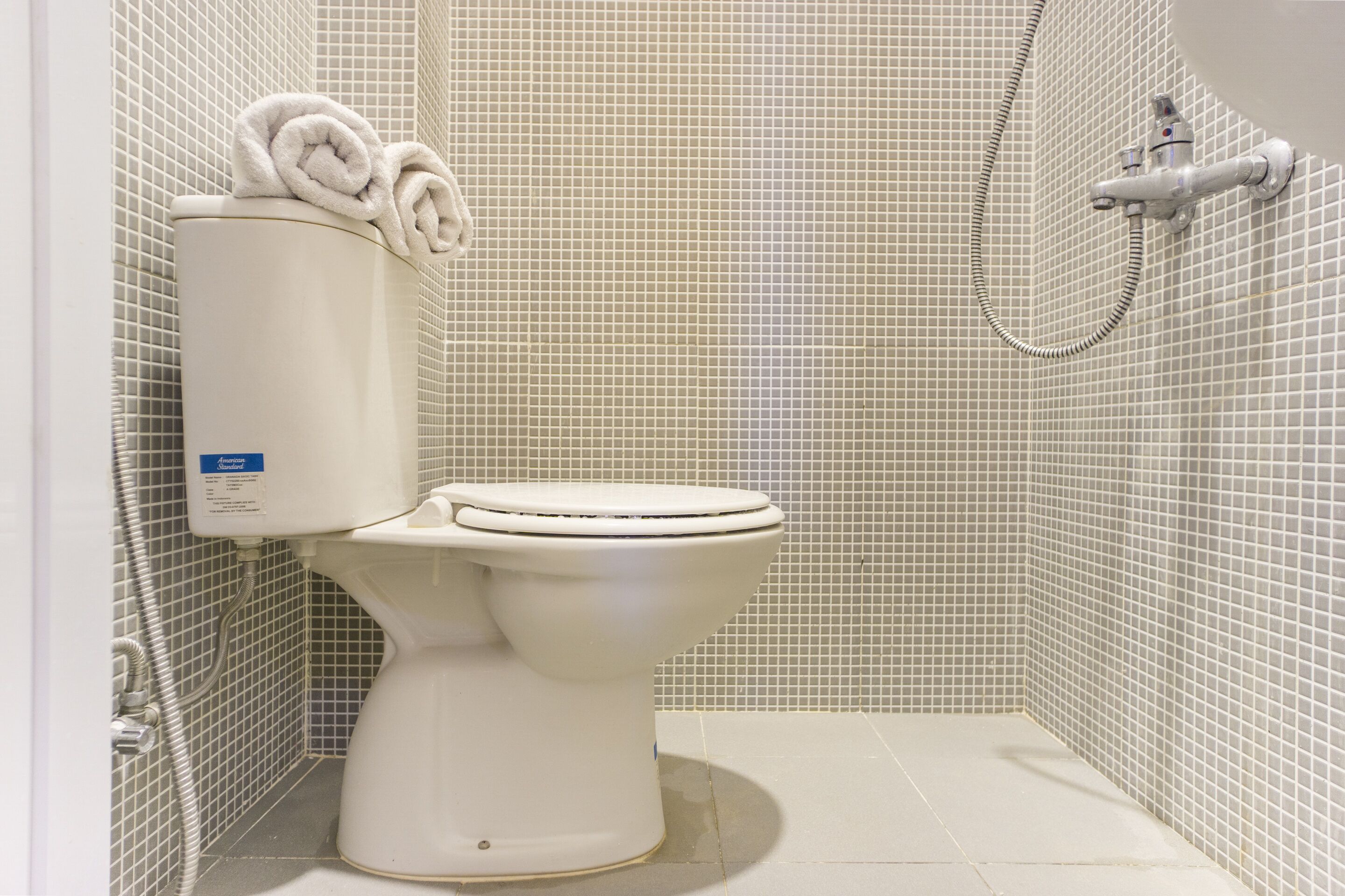 A white toilet with a control panel and a shower head in a tiled bathroom.