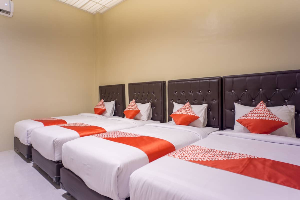 A hotel room with four beds, each with white bedding and orange accents.
