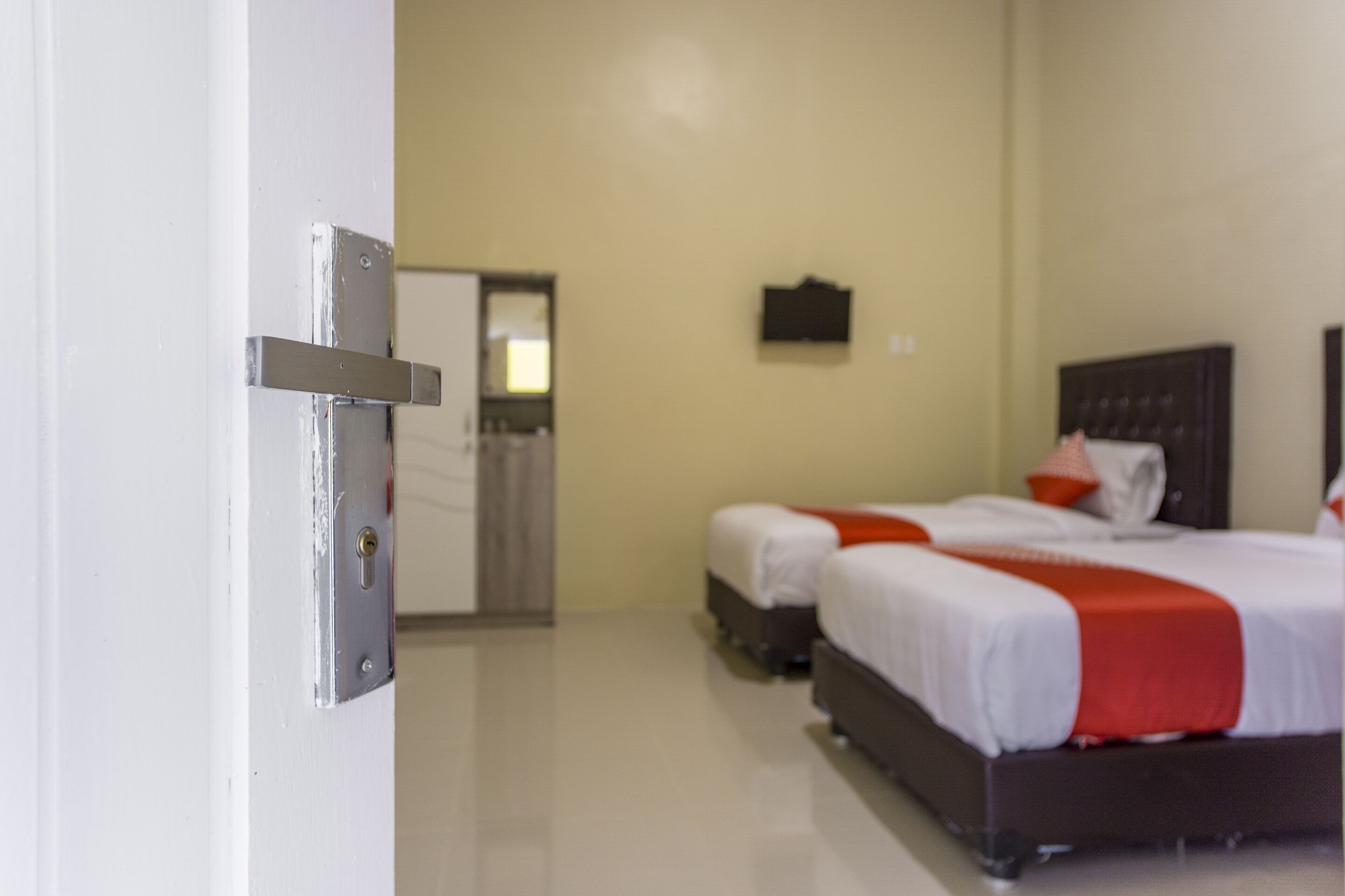 A hotel room with two beds, a wardrobe, and a door with a handle.