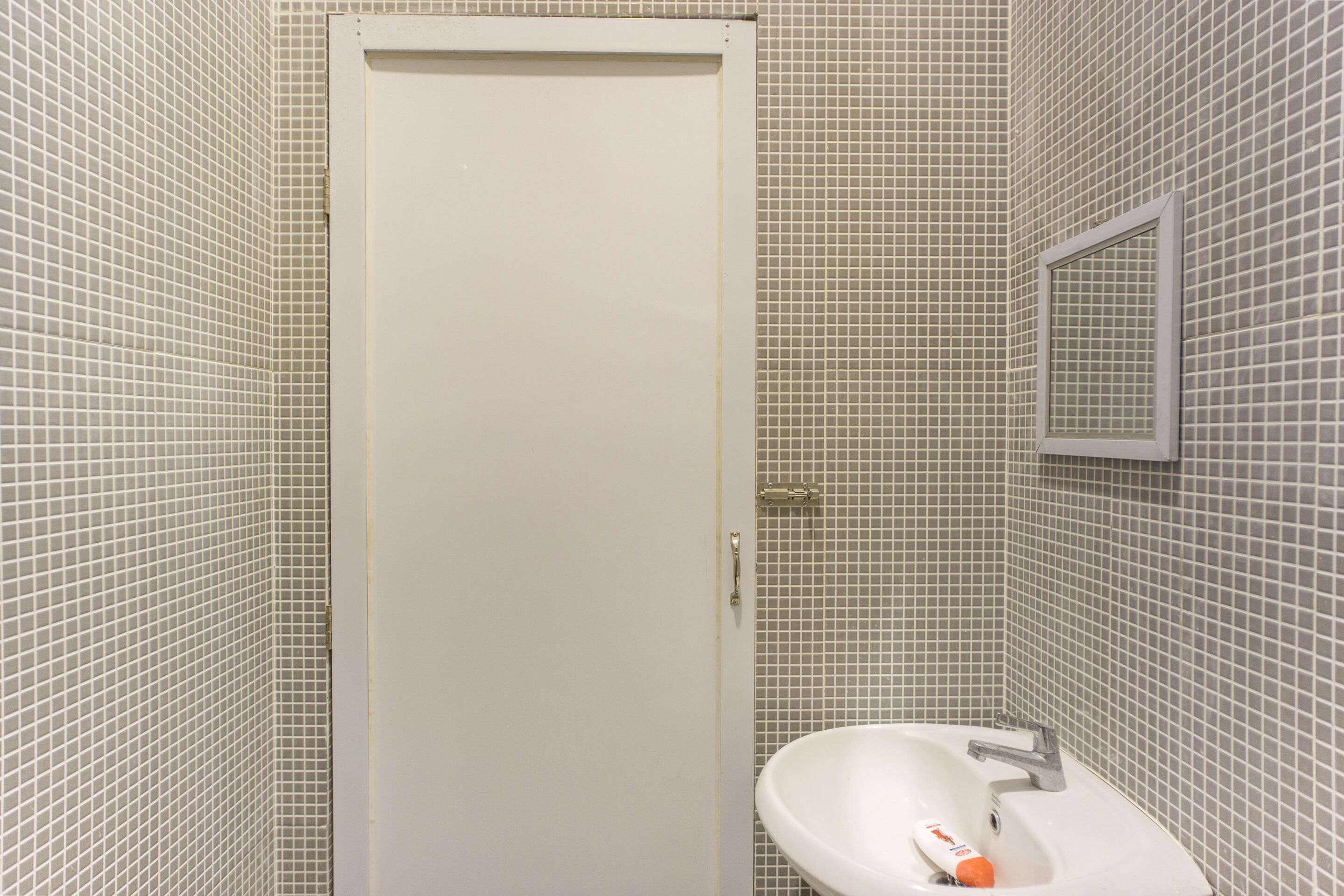A bathroom with a white door, a sink with a mirror, and tiled walls.