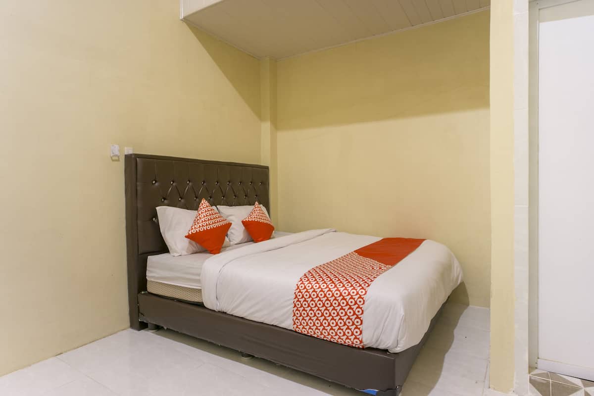 A single bed with a brown headboard, white bedding, and orange decorative pillows.
