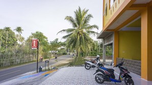 Uma área pavimentada com duas scooters estacionadas, uma estrada com alguns veículos e uma placa.