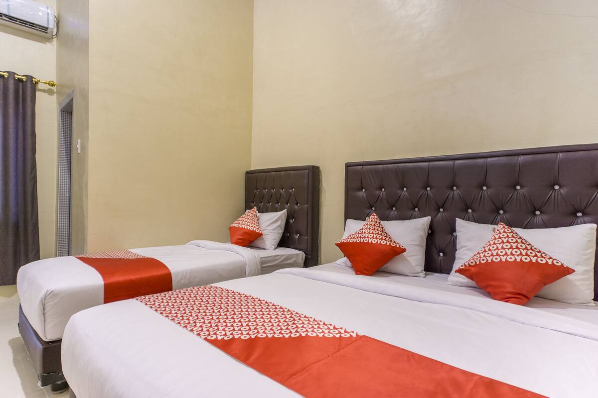 Two double beds with red and white bedding, a dark headboard, and a small bedside table with a lamp.