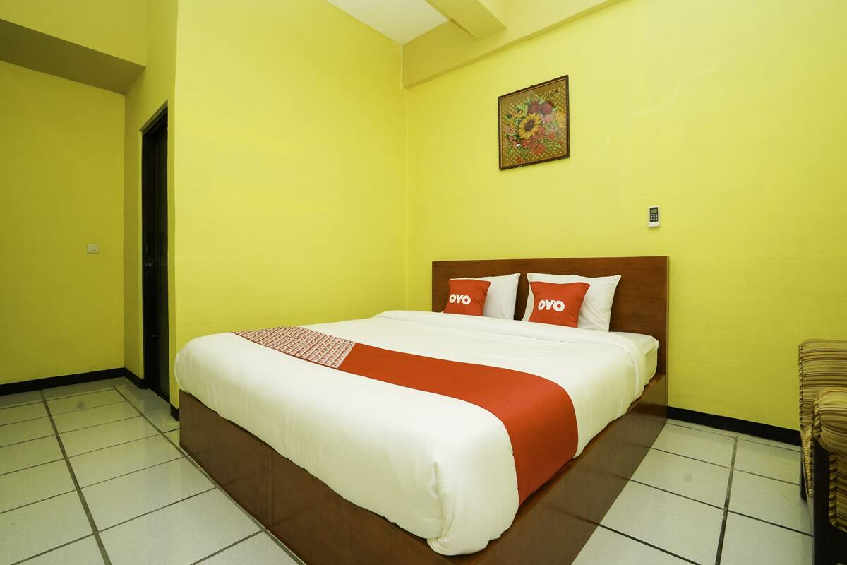 A hotel room with a bed, a painting on the wall, and a chair.