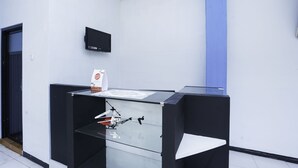 Een receptiebalie met een wandtelevisie, een glazen vitrine en een blauwe pilaar.