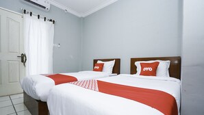 Een hotelkamer met twee bedden, witte beddengoed, rode accenten en een witte deur met gordijn.