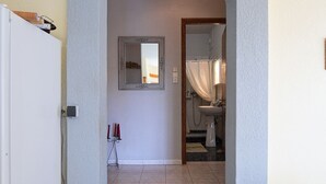 A hallway leading to a bathroom with a shower curtain, a mirror, and a tiled floor.