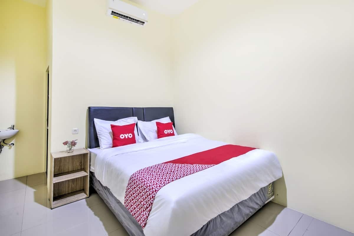 Ein Hotelzimmer mit einem Bett, einem Nachttisch, einer Wand-Klimaanlage und einer kleinen Vase mit Blumen.