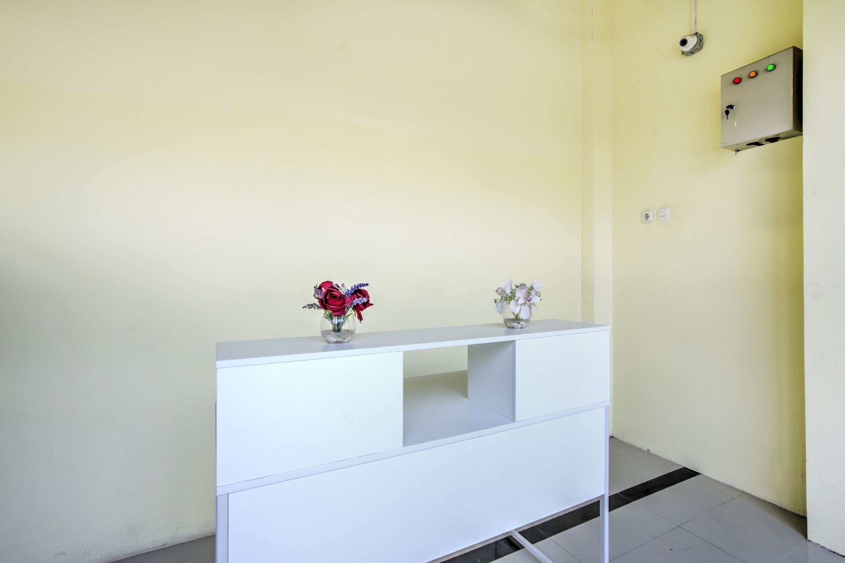 A white console table with two vases of flowers, a security camera, and a control panel on the wall.