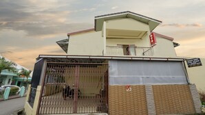 Un edificio de dos pisos con balcón, entrada protegida por un portón y un cartel con la dirección.