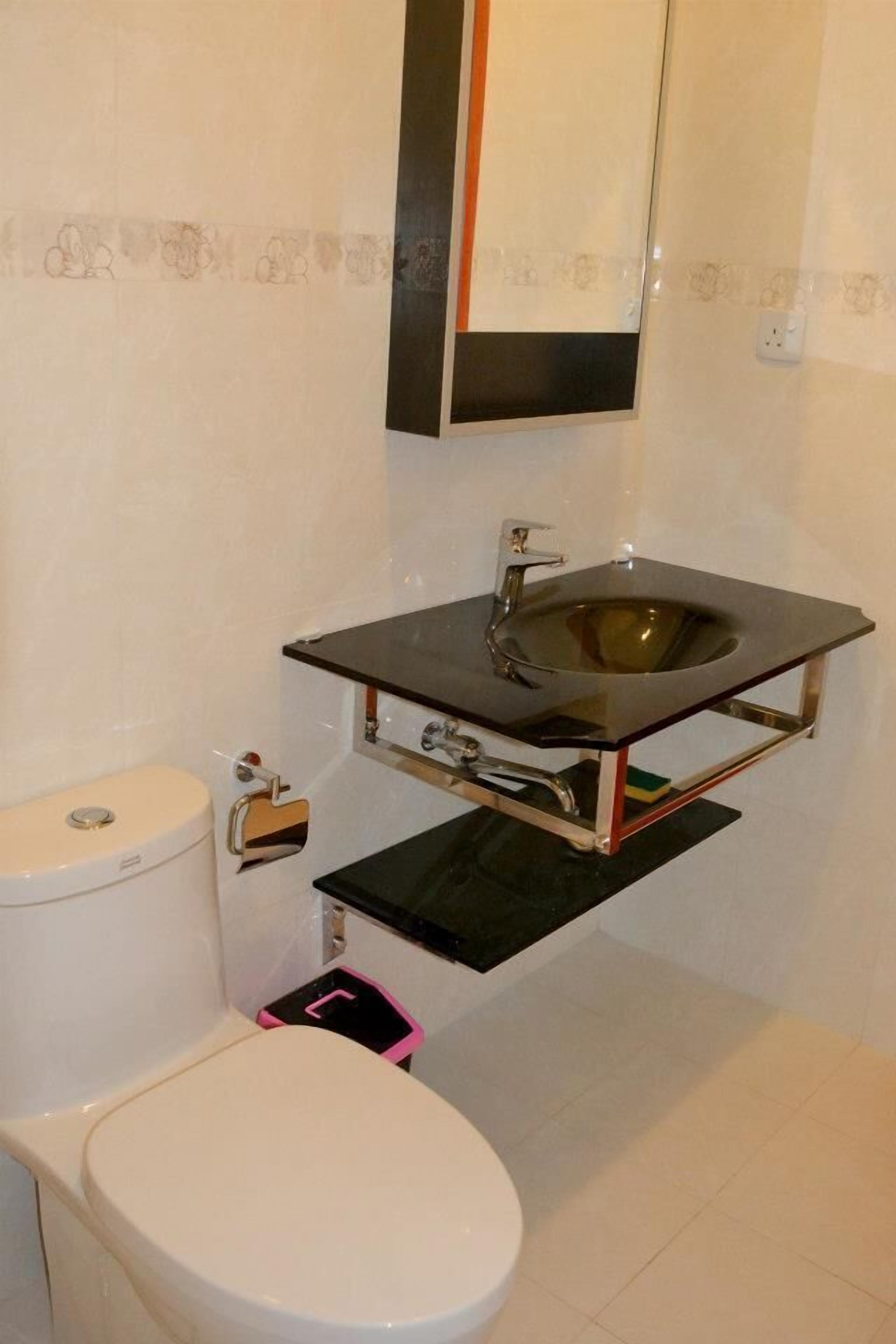 Un baño con inodoro blanco, lavamanos negro y un espejo encima, además de un pequeño cubo de basura.