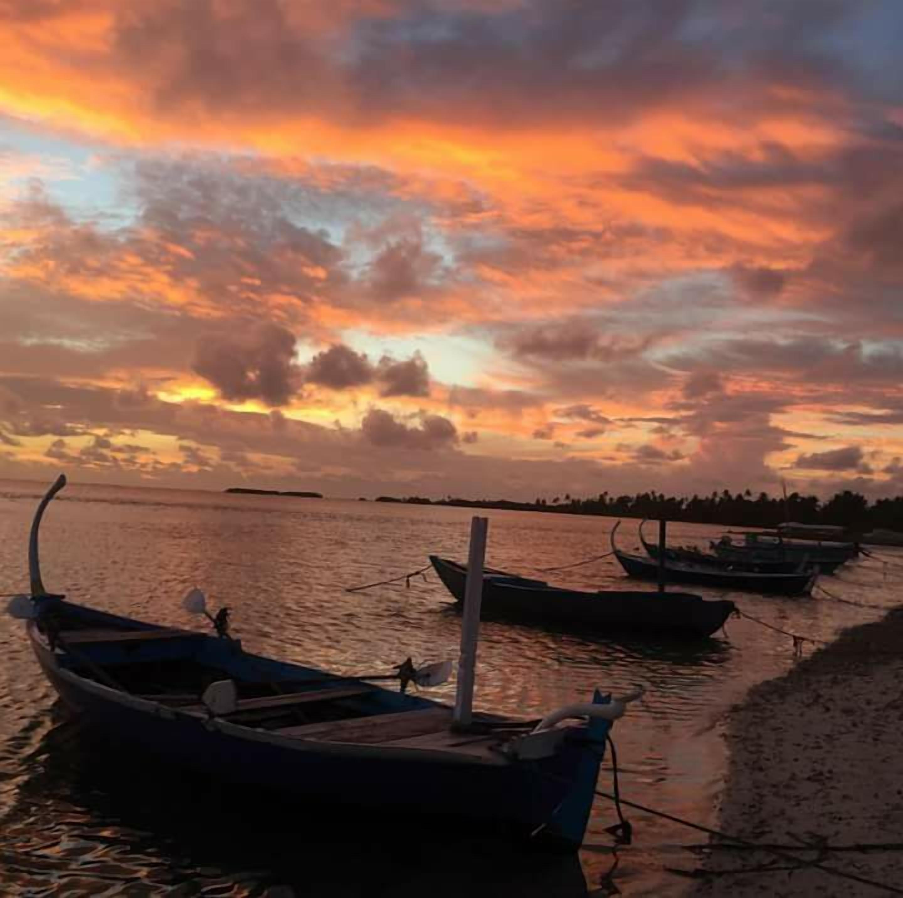Un atardecer sobre una superficie acuática tranquila con barcos amarrados a la orilla.