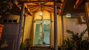 A building entrance with a wooden porch, a glass door, and potted plants. - Charming Holiday Lodge (Hulhudhoo)