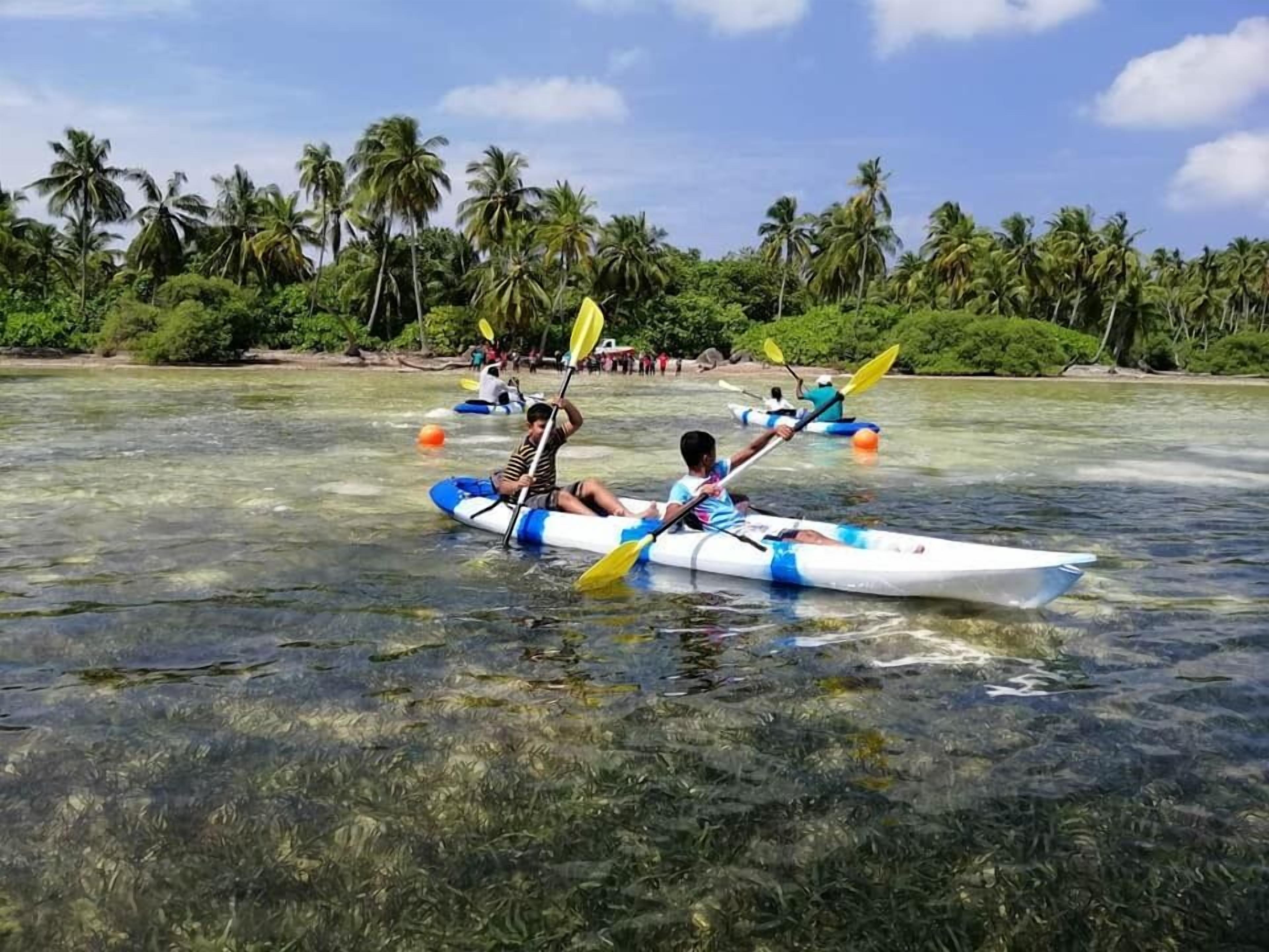 A clear tropical waterway with kayaks and a beach lined with palm trees.