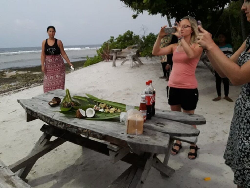 Preparación para un picnic en la playa, con una mesa de madera, comida y bebidas.
