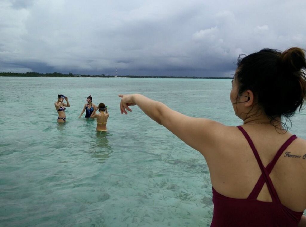 A woman in a red swimsuit pointing towards three other people in the water.