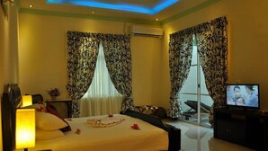 A hotel room with a bed, a TV, a desk, and curtains. - Charming Holiday Lodge (Hulhudhoo)