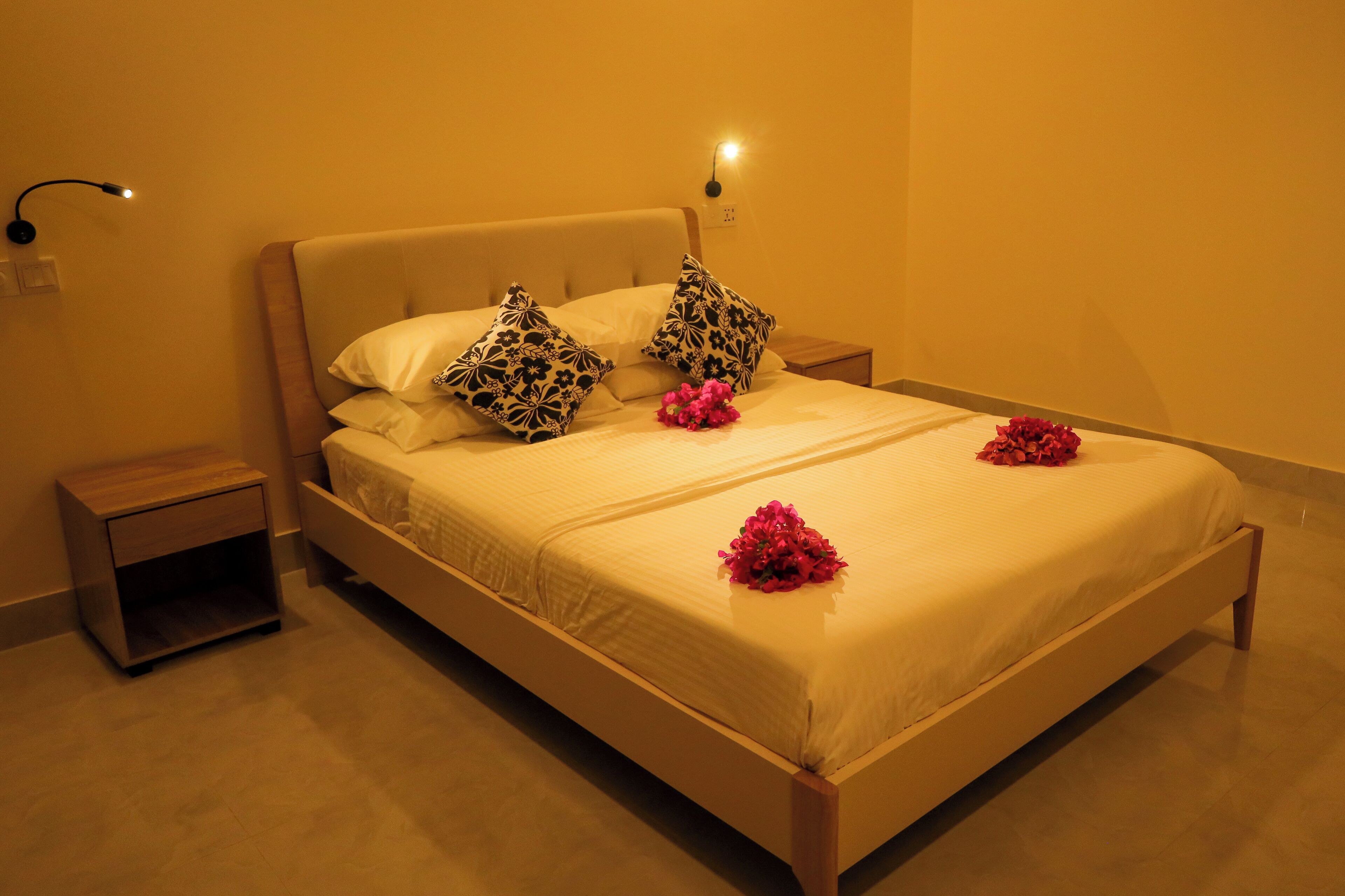 A neatly made bed with floral pillows and a bouquet of flowers.
