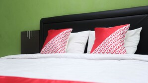 A bed with white and red bedding, a black headboard, and green walls.