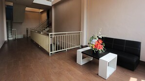 A spacious lobby with a staircase, a black sofa, a white coffee table, and a floral arrangement.