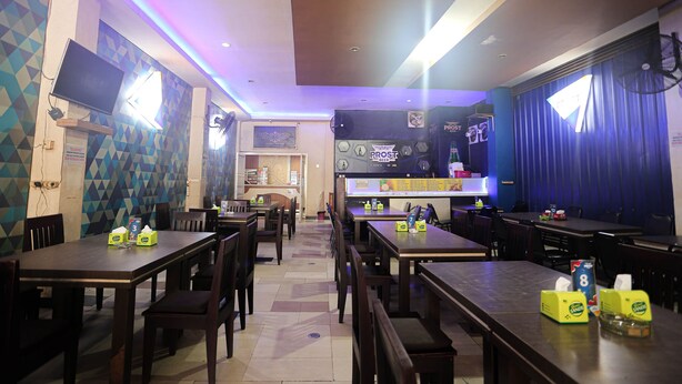 A restaurant with multiple tables and chairs, a counter with a menu, and a wall-mounted TV.
