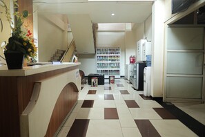 Un espace d’accueil comprenant un comptoir, une plante en pot, un escalier, une étagère avec divers objets et un réfrigérateur.