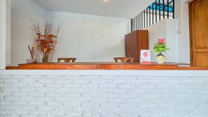 A reception area with a white brick wall, wooden reception desk, two chairs, a staircase with a black railing, and a door. - OYO 2519 Mayang Garini (Borobudur)