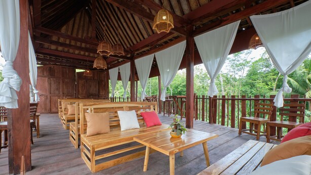 A wooden deck with benches and tables, surrounded by a wooden fence, and overlooking a lush green landscape. - OYO 2519 Mayang Garini (Borobudur)