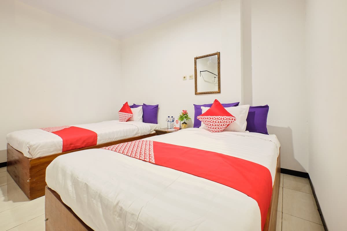 A hotel room with two beds, each with white bedding and red accents, a small table with a plant, and a mirror on the wall.