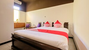 A neatly made bed with a white and red bedspread, a wooden headboard, and a small table with a purple chair beside it. - OYO 2519 Mayang Garini (Borobudur)