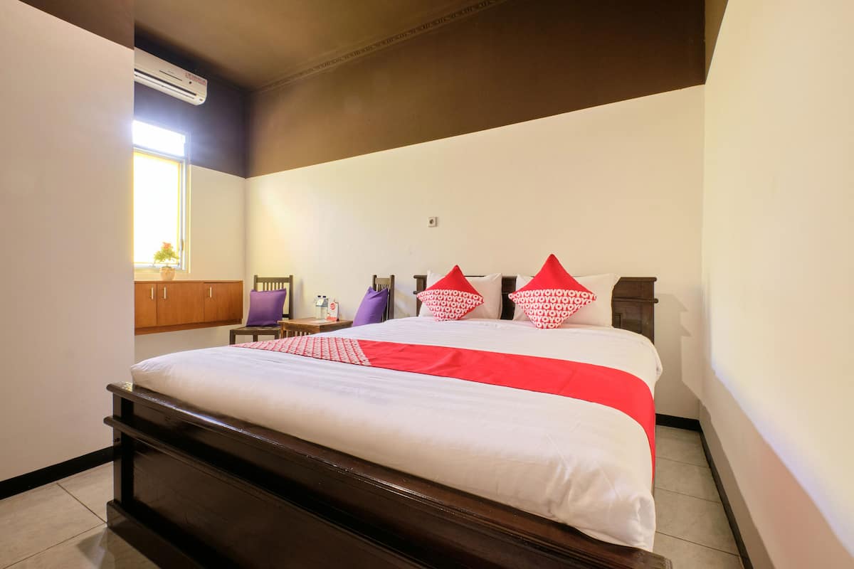 A neatly made bed with a white and red bedspread, a wooden headboard, and a small table with a purple chair beside it.