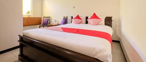 A neatly made bed with a white and red bedspread, a wooden headboard, and a small table with a purple chair beside it.