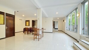 A spacious room with a dining area featuring a table and chairs, a wooden door, and large windows with a view of greenery outside. - OYO 2519 Mayang Garini (Borobudur)