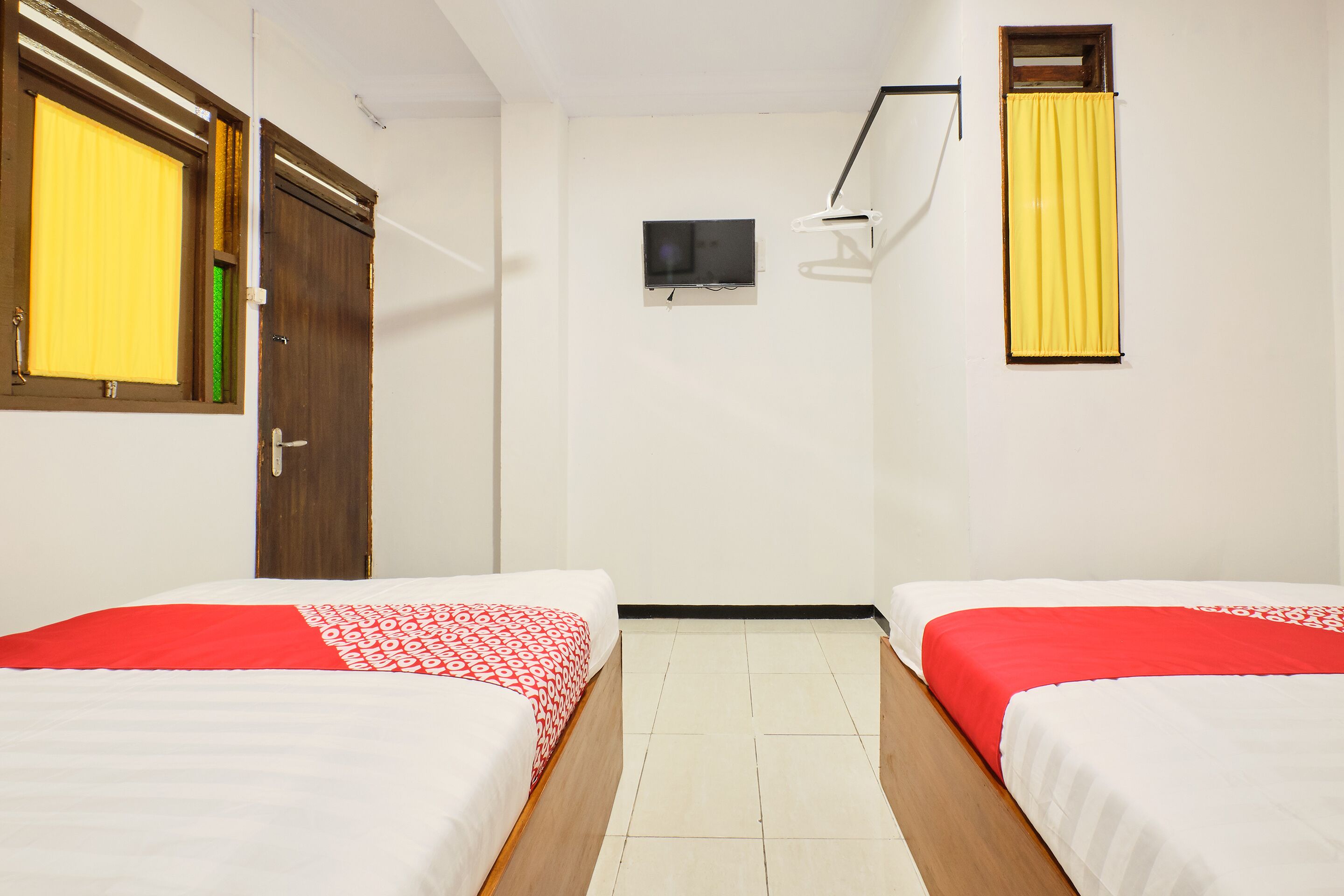 A hotel room with two beds, a television, and a window with yellow curtains.