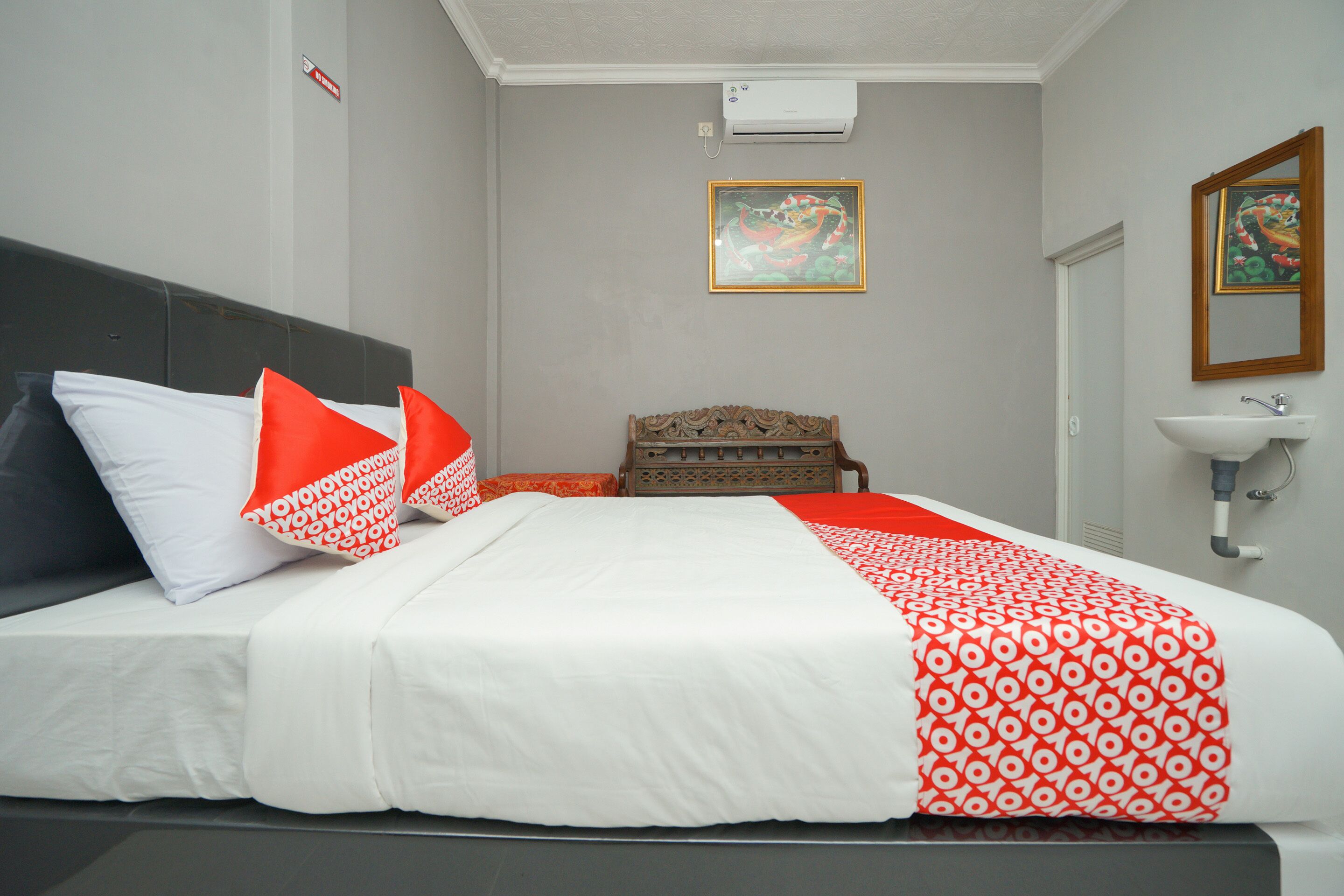 Una habitación de hotel con una cama, un cabecero de madera, una pequeña silla de madera, un lavabo blanco y una obra de arte enmarcada en la pared.