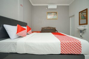A hotel room with a bed, a wooden headboard, a small wooden chair, a white sink, and a framed artwork on the wall. - OYO 2492 Nindy Homestay (Probolinggo)