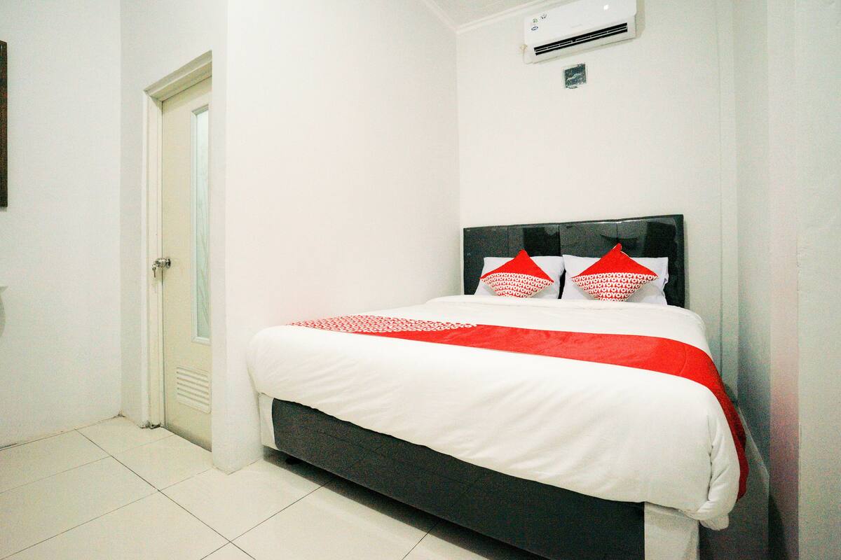 A bedroom with a bed, white walls, a door, and an air conditioning unit.