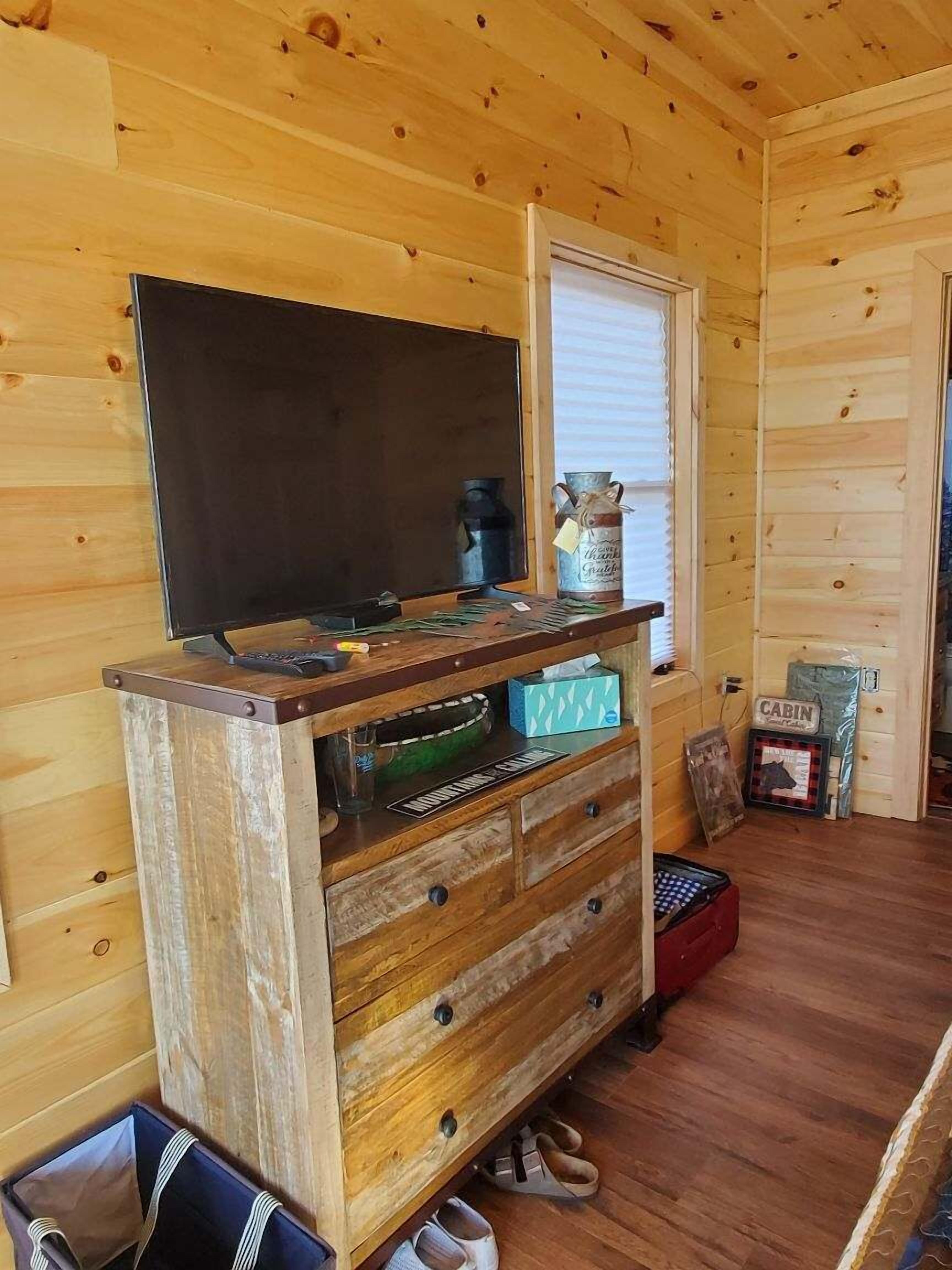 A wooden cabin interior with a TV on a wooden stand, a window, a wooden cabinet with drawers, and a 'CABIN' sign.