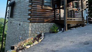 A log cabin with a stone foundation, a porch, and a small garden area with rocks and plants. - Princesses Mountain View ,  Romantic/Honeymoon getaway   (Sevierville)