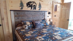 A wooden bedroom with a bed, two pillows, a nightstand, and a wall with a bear and tree design. - Princesses Mountain View ,  Romantic/Honeymoon getaway   (Sevierville)