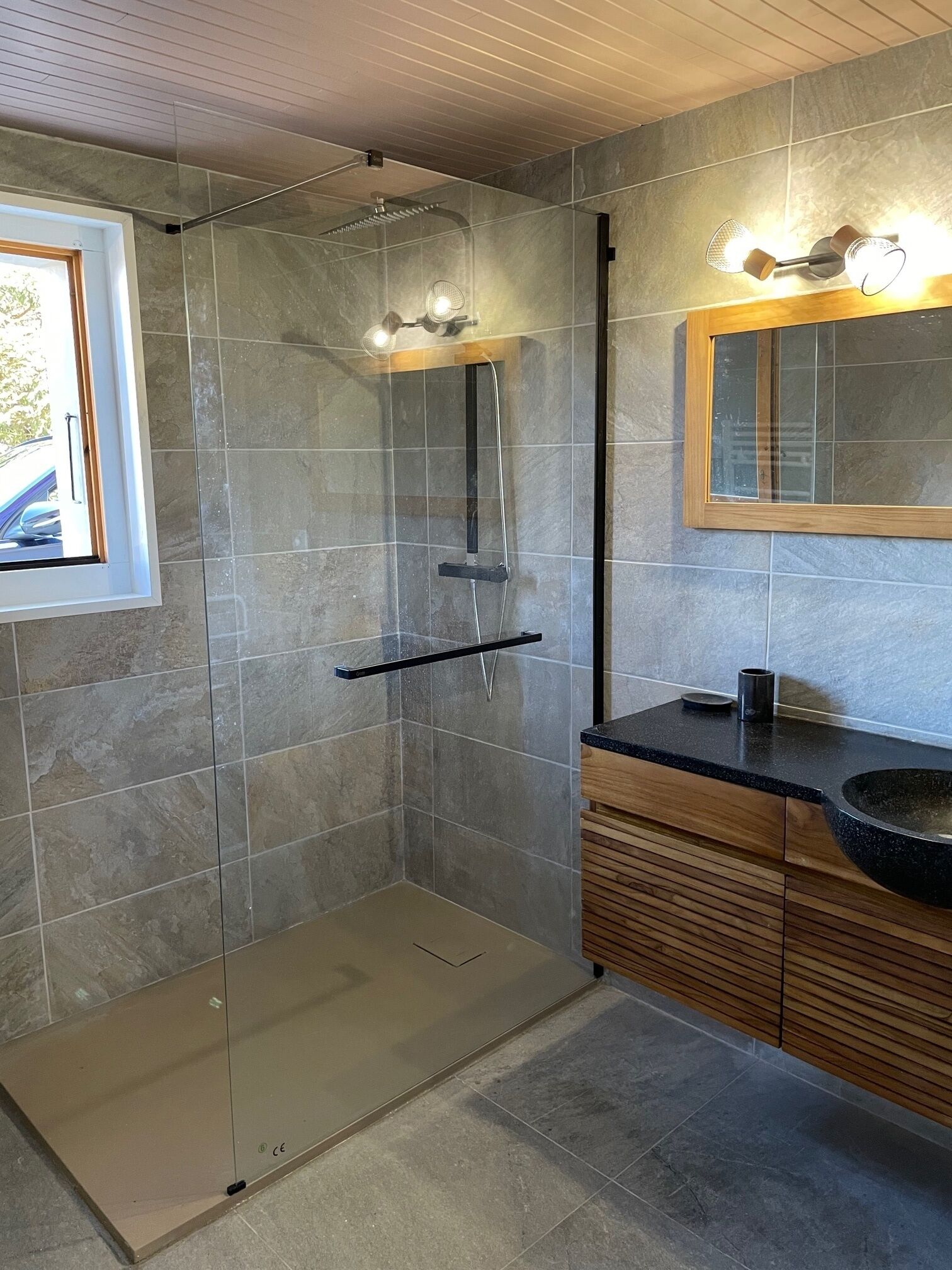 Une salle de bain moderne avec une douche à parois de verre, un meuble-lavabo en bois et un grand miroir.
