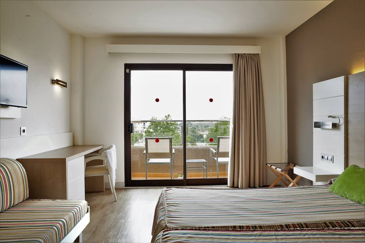 A modern hotel room with a bed, a desk, and a balcony with a view.