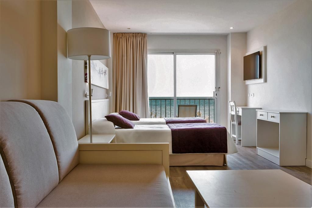 A hotel room with two beds, a desk, a TV, and a balcony with a view.