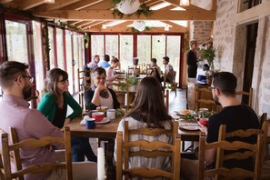 A dining area with wooden tables and chairs, large windows, and a rustic stone wall. - Hotel Le Morimont (Oberlarg)