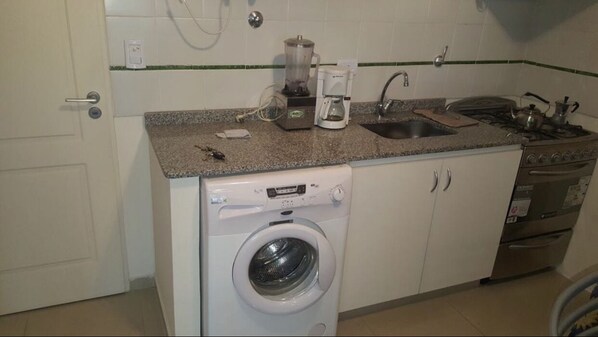 A compact kitchen with a washing machine, coffee maker, and stove. - La Martina 2 (Haedo)